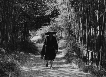 Movie still from “Rashomon” (1950), directed by Akira Kurosawa – An older woman walking down a path in the woods; Wide shot, High angle