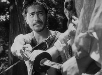 Movie still from “Rashomon” (1950), directed by Akira Kurosawa – A black - and - white photo of a man holding a sword; Close Up shot, Over the shoulder angle