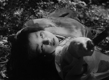 Movie still from “Rashomon” (1950), directed by Akira Kurosawa – A young woman laying on the ground holding a gun; Close Up shot, High angle