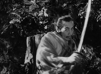 Movie still from “Rashomon” (1950), directed by Akira Kurosawa – A man holding a bow and arrow in the woods; Medium shot, Low angle