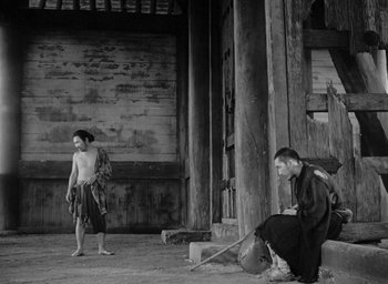 Movie still from “Rashomon” (1950), directed by Akira Kurosawa – A man sitting on steps next to another man; Wide shot, High angle