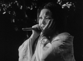 Movie still from “Rashomon” (1950), directed by Akira Kurosawa – A woman holding a wooden stick in front of her face; Close Up shot, Low angle