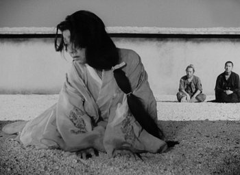 Movie still from “Rashomon” (1950), directed by Akira Kurosawa – A woman sitting on the ground in front of a man; Wide shot, Low angle