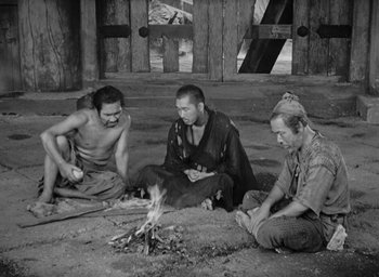 Movie still from “Rashomon” (1950), directed by Akira Kurosawa – A group of men sitting around a fire; Wide shot, High angle
