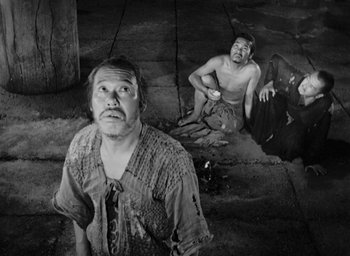 Movie still from “Rashomon” (1950), directed by Akira Kurosawa – A man standing next to another man on the ground; Wide shot, High angle