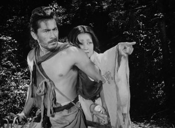 Movie still from “Rashomon” (1950), directed by Akira Kurosawa – A man and a woman are standing in the woods; Medium shot, Low angle