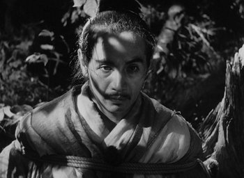 Movie still from “Rashomon” (1950), directed by Akira Kurosawa – A black and white photo of a man tied to a tree; Close Up shot, High angle
