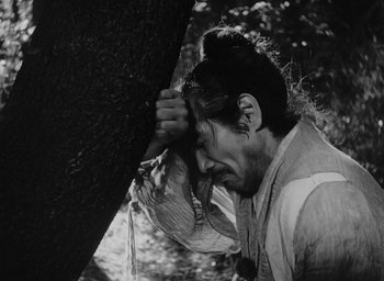 Movie still from “Rashomon” (1950), directed by Akira Kurosawa – A man holding his head against the side of a tree; Close Up shot, High angle