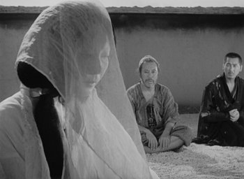 Movie still from “Rashomon” (1950), directed by Akira Kurosawa – A man and a woman sitting on the ground in front of a wall; Medium shot, Low angle