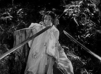 Movie still from “Rashomon” (1950), directed by Akira Kurosawa – A woman holding two swords in a forest; Medium shot, Low angle