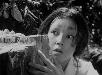 Movie still from “Rashomon” (1950), directed by Akira Kurosawa – A young woman holding a piece of wood in front of her face; Close Up shot, Low angle