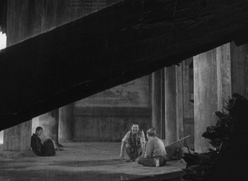 Movie still from “Rashomon” (1950), directed by Akira Kurosawa – A group of people sitting on the ground in an open area; Wide shot, High angle
