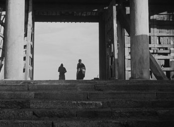 Movie still from “Rashomon” (1950), directed by Akira Kurosawa – Two people are standing on the steps of a pier; Extreme Wide shot, Low angle