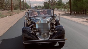 Movie still from “Rat Race” (2001), directed by Jerry Zucker – A group of people riding in the back of an antique car; Wide shot, Low angle