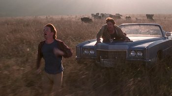 Movie still from “Rat Race” (2001), directed by Jerry Zucker – A man and a woman in a field near a car; Wide shot, Low angle
