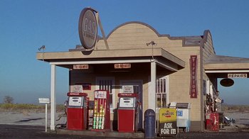 Movie still from “Rat Race” (2001), directed by Jerry Zucker – An old gas station with several pumps on the side of the road; Extreme Wide shot, Low angle