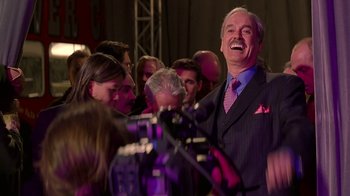 Movie still from “Rat Race” (2001), directed by Jerry Zucker – A man in a suit and tie laughing at an event; Medium shot, Low angle