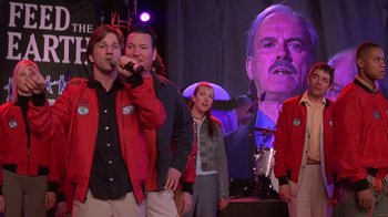 Movie still from “Rat Race” (2001), directed by Jerry Zucker – A group of young people singing in front of an image of an older man; Medium shot, Low angle