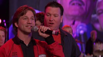 Movie still from “Rat Race” (2001), directed by Jerry Zucker – A man is holding a microphone up to his mouth; Close Up shot, Over the shoulder angle