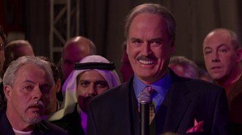 Movie still from “Rat Race” (2001), directed by Jerry Zucker – A man that is standing in front of a microphone; Close Up shot, Over the shoulder angle