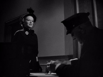 Movie still from “Raw Deal” (1948), directed by Anthony Mann – A woman wearing a hat and gloves standing next to a man; Medium shot, Low angle
