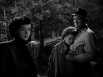 Movie still from “Raw Deal” (1948), directed by Anthony Mann – A man and a woman standing next to each other in a forest; Medium shot, High angle