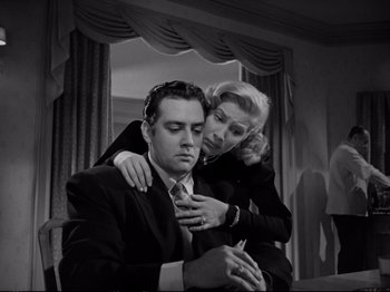 Movie still from “Raw Deal” (1948), directed by Anthony Mann – A man and a woman in a suit and tie in front of a window; Medium shot, Low angle