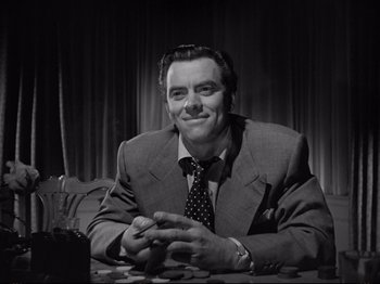 Movie still from “Raw Deal” (1948), directed by Anthony Mann – A black and white photo of a man sitting at a table; Medium shot, Low angle
