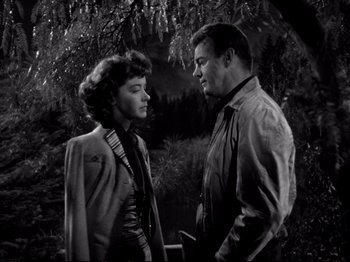 Movie still from “Raw Deal” (1948), directed by Anthony Mann – A man and a woman standing next to each other in front of a tree; Medium shot, High angle