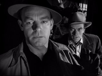 Movie still from “Raw Deal” (1948), directed by Anthony Mann – A man in a hat and a man in a trench coat and a hat; Close Up shot, Low angle