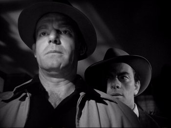 Movie still from “Raw Deal” (1948), directed by Anthony Mann – A man and a man wearing a hat and a trench coat; Close Up shot, Low angle