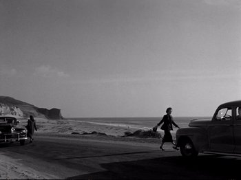 Movie still from “Raw Deal” (1948), directed by Anthony Mann – A woman walking down the street near a car; Extreme Wide shot, Low angle