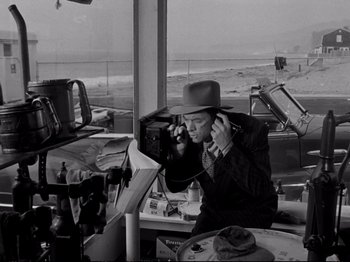 Movie still from “Raw Deal” (1948), directed by Anthony Mann – A man wearing a cowboy hat is talking on a phone; Medium shot, Over the shoulder angle