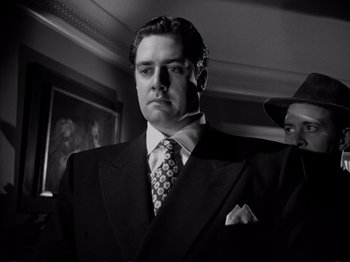 Movie still from “Raw Deal” (1948), directed by Anthony Mann – Black and white photograph of a man in a suit and tie; Close Up shot, Low angle