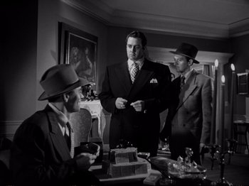 Movie still from “Raw Deal” (1948), directed by Anthony Mann – A group of men standing around a table with a cake on it; Medium shot, Low angle