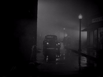Movie still from “Raw Deal” (1948), directed by Anthony Mann – A black and white photo of a car on a rainy night; Extreme Wide shot, High angle