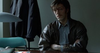 Movie still from “Read My Lips” (2001), directed by Jacques Audiard – A man sitting at a table with his arms crossed; Close Up shot, Over the shoulder angle