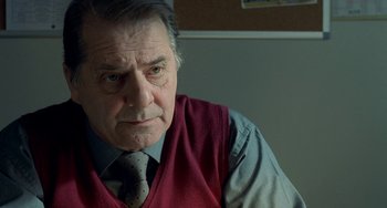 Movie still from “Read My Lips” (2001), directed by Jacques Audiard – An older man wearing a red vest and a tie; Close Up shot, Over the shoulder angle
