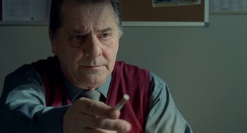 Movie still from “Read My Lips” (2001), directed by Jacques Audiard – An older man is holding a cigarette in his hand; Close Up shot, High angle