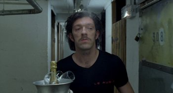 Movie still from “Read My Lips” (2001), directed by Jacques Audiard – A man with long black hair holding a bucket of champagne; Close Up shot, Low angle