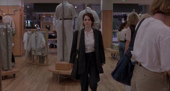 Movie still from “Reality Bites” (1994), directed by Ben Stiller – A woman in a black suit and white shirt is standing in front of some people; Medium shot, Over the shoulder angle