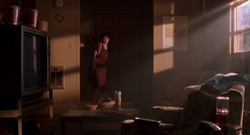 Movie still from “Reality Bites” (1994), directed by Ben Stiller – A woman standing in a living room with a bowl on the table; Wide shot, Over the shoulder angle