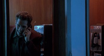 Movie still from “Reality Bites” (1994), directed by Ben Stiller – A man sitting in front of a window talking on a phone; Medium shot, Low angle