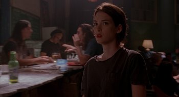 Movie still from “Reality Bites” (1994), directed by Ben Stiller – A woman standing in front of a group of people at a table; Medium shot, Over the shoulder angle