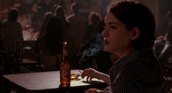 Movie still from “Reality Bites” (1994), directed by Ben Stiller – A woman sitting in front of a bottle of beer; Close Up shot, Over the shoulder angle