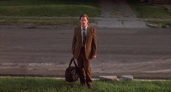 Movie still from “Reality Bites” (1994), directed by Ben Stiller – A man in a suit and tie holding a bag; Wide shot, Low angle