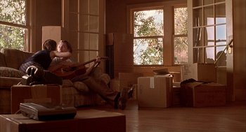 Movie still from “Reality Bites” (1994), directed by Ben Stiller – A man sitting on a couch playing a guitar; Wide shot, Low angle