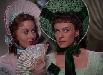 Movie still from “Reap the Wild Wind” (1942), directed by Cecil B. DeMille – Two beautiful women in fancy hats holding fans; Close Up shot, Over the shoulder angle