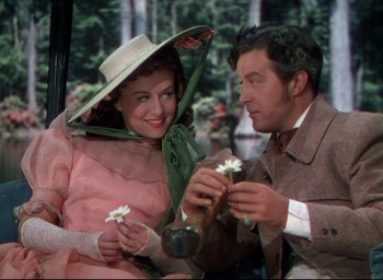 Movie still from “Reap the Wild Wind” (1942), directed by Cecil B. DeMille – A man and a woman sitting next to each other holding flowers; Medium shot, Over the shoulder angle
