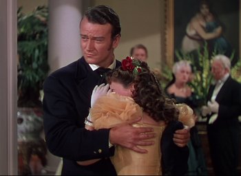 Movie still from “Reap the Wild Wind” (1942), directed by Cecil B. DeMille – A man and a woman hugging in a room with other people; Medium shot, Over the shoulder angle